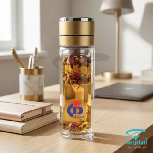 فلاسک دمنوشساز پیرکس دوجداره M2020 با درب فلزی طلایی و چاپ لوگوی بیمه دانا حاوی دمنوش گیاهی روی میز کار.